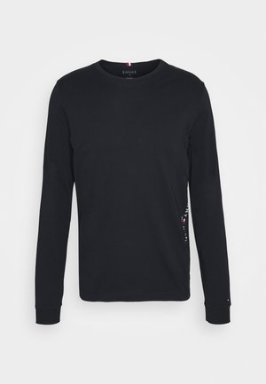 Sort langærmet crewneck skjorte med diskret logo på ærmet, lavet af blødt stof, vist på en ensfarvet hvid baggrund.