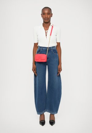 Top alb cu dungi, cu detalii cu șnur, pantaloni răspândiți din denim albastru, geantă mică de umăr roșie cu lanț de aur și pantofi negri cu vârf ascuțit.