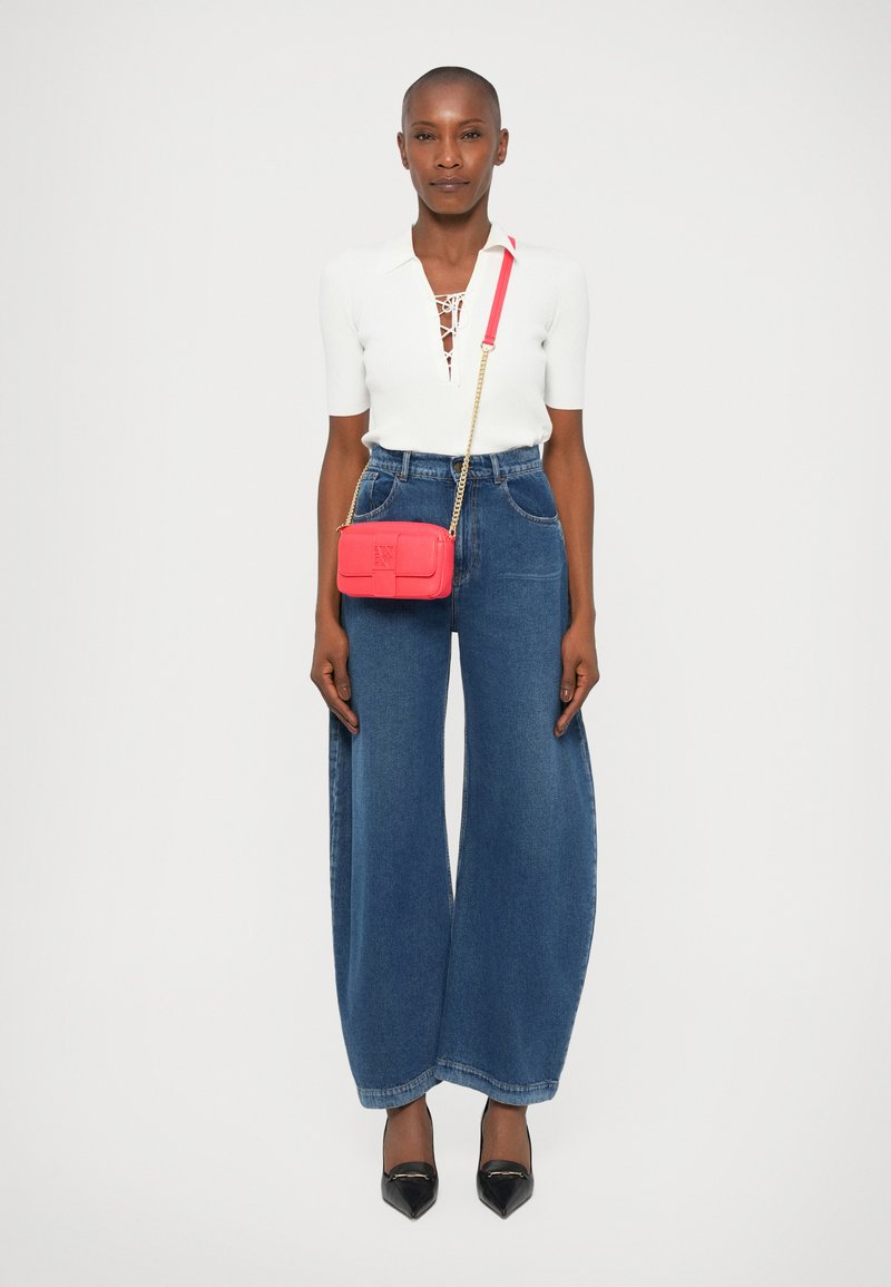 Biały prążkowany top z detalem sznurowania, szerokie niebieskie dżinsowe spodnie, mała czerwona torebka crossbody ze złotym łańcuchem oraz czarne szpilki w szpic.