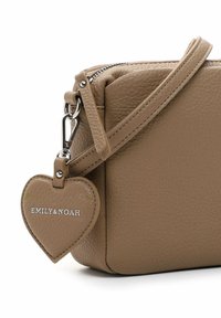 Brown leather crossbody bag with a textured finish, featuring a heart-shaped tag and a silver zipper. Adjustable strap included.