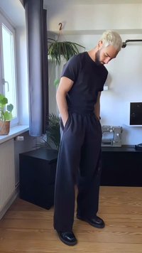 Zwarte t-shirt met korte mouwen en brede zwarte broek. Gladde stof met een elastische tailleband. Staande in een heldere binnenomgeving.