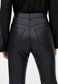 Pantalons taille haute en simili cuir noir avec poches cousues et texture lisse, présentant un design ajusté au niveau de la taille et des hanches.
