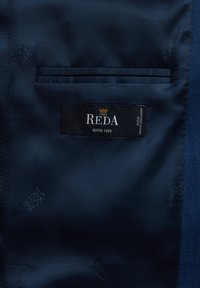 Granatowy materiał o gładkiej fakturze, z wewnętrzną kieszenią i metką z napisem "REDA SUPER 130’S." Delikatne logo obecne.