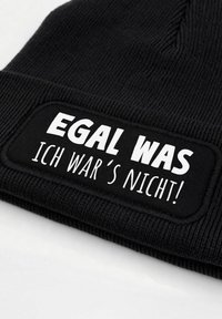 Black knitted beanie with a rectangular fabric patch displaying the text "EGAL WAS ICH WAR'S NICHT!" in bold white font.