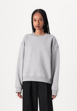 Gray sweatshirt made of soft fabric, featuring a relaxed fit, wide sleeves, and ribbed cuffs. Paired with black loose-fitting pants.