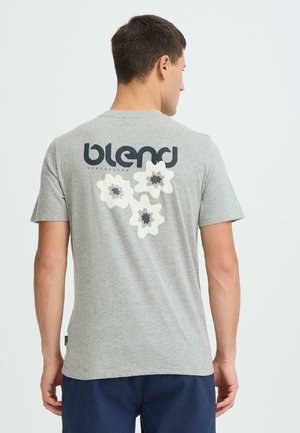 T-shirt gris à manches courtes avec un grand logo "blend" et trois motifs floraux blancs au dos. Tissu doux, coupe décontractée, et aucun motif à l'avant.