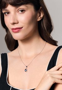 Srebrny naszyjnik z kroplą niebieskiego kamienia szlachetnego, ozdobiony akcentem diamentowym. Noszony na odkrytej szyi, eksponuje misterny wzór.