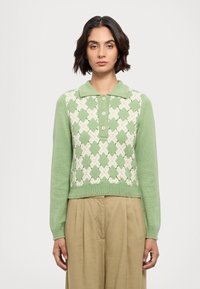 Lys grøn sweater med krave, prydet med et diamantmønster i hvid og mørkere grøn, lange ærmer og en cropped design.