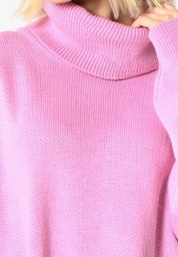 Růžový rolákový svetr s žebrovaným límcem a texturovaným úpletem. Má dlouhé, volné rukávy a měkký, útulný vzhled.