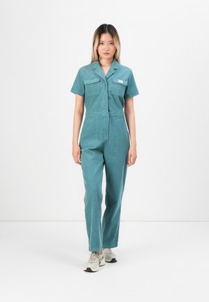 Teal jumpsuit with short sleeves, two chest pockets, a front zipper, and tapered legs. Made of textured cotton blend fabric.