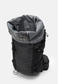 Sac à dos noir avec une fermeture à enrouler grise. Comprend des bretelles réglables, une poche latérale et des instructions d'entretien imprimées à l'intérieur de l'ouverture.