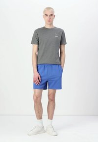 Gray cotton T-shirt with a small logo, paired with blue athletic shorts. Model wears white sneakers and crew-length socks.