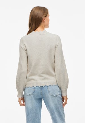 Light gray sweater with long sleeves, scalloped neckline, and textured hem. Paired with blue high-waisted jeans. Soft knit material.