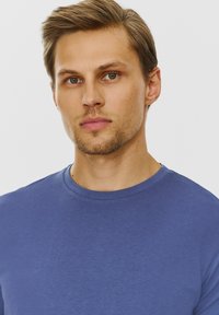 Niebieska koszulka z krótkim rękawem z bawełny z okrągłym dekoltem. Gładka faktura i dopasowany krój, cechująca się jednolitym kolorem bez wzorów czy akcentów.