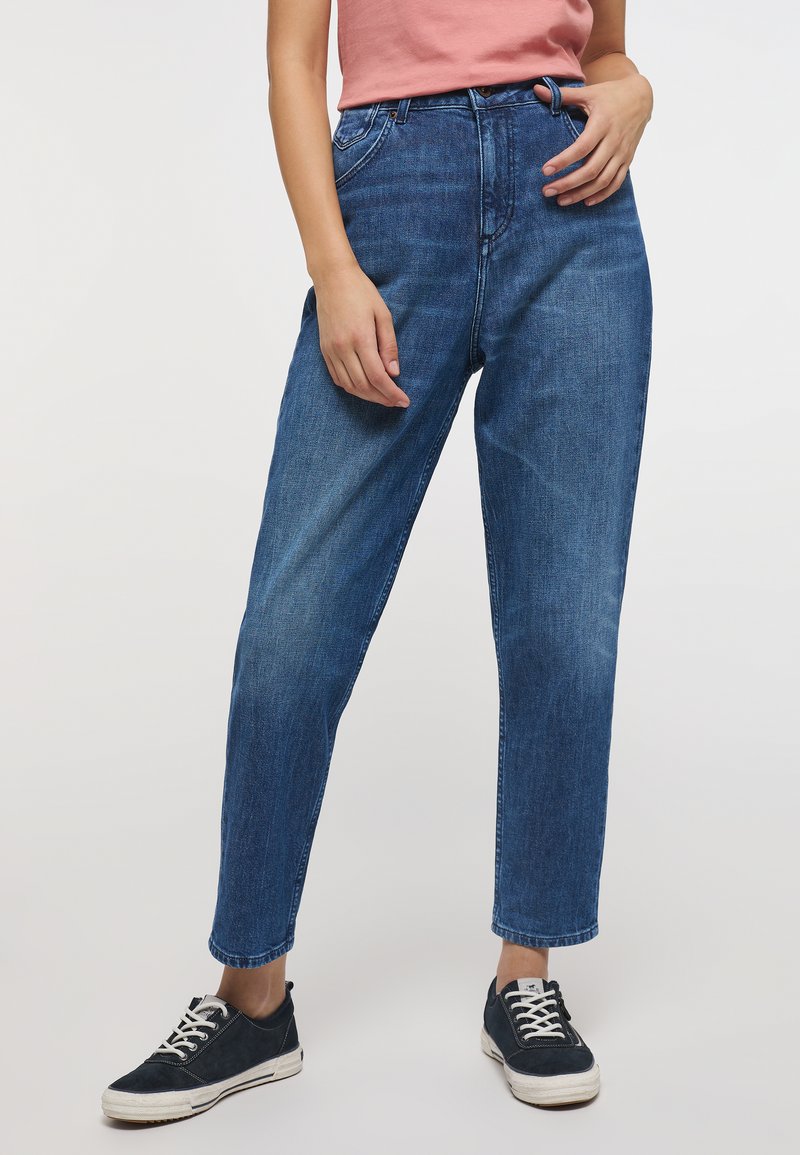 Jeans de mezclilla de un azul claro con una cintura alta, pierna recta y un ligero desgaste. Combinados con zapatillas deportivas navy y una blusa rosa.