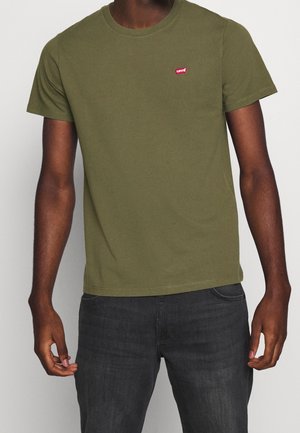 Homme portant un t-shirt Levi's vert olive à manches courtes et col rond, ainsi qu'un jean gris foncé, debout devant un fond clair uni.