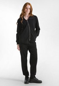 Schwarzer Zip-Up-Sweatshirt mit hohem Kragen, kombiniert mit passenden schwarzen Hosen. Der Stoff wirkt weich mit einer glatten Textur; beide haben minimale Akzente.