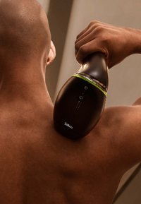 Black handheld device with a curved shape and green accent, positioned against a skin-toned back, featuring control buttons and branding.