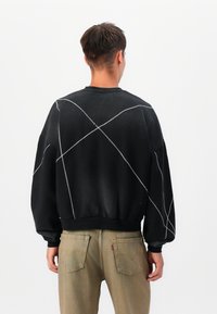 Schwarzer Pullover mit übergroßer Passform, gerippten Bündchen und Saum. Verfügt über kontrastierende weiße Nähte in einem Kreuzmuster auf der Rückseite.