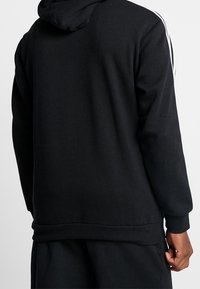 Svart luvtröja med mjuk textur, med vita sidoränder, avslappnad passform och ribbad kant och mudd för komfort.