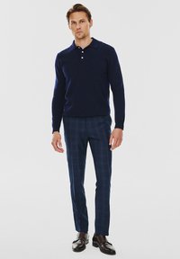 Granatowa koszula polo z długim rękawem z trzema guzikami, w połączeniu z niebieskimi spodniami w kratę i ciemnobrązowymi skórzanymi butami.