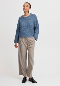 Sininen valloittava neulepusero pitkillä hihoilla, yhdistettynä beigeihin raitapaitoisiin leveälahkeisiin housuihin ja mustiin nahkaisiin loafereihin.