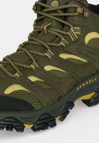 Πράσινο και κίτρινο μποτάκι πεζοπορίας Merrell με υψηλή γάμπα, υφασμάτινο με υφή, ανθεκτική σόλα και μοτίβο στους κίτρινους και γκρι κορδόνια.