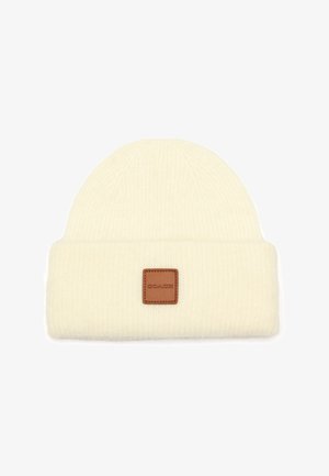 Bonnet en tricot crème avec un revers, arborant une étiquette en cuir carrée sur le devant. Tissu texturé et extensible.