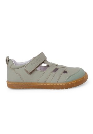 Sandale enfant en cuir gris clair avec bride velcro, découpes latérales ouvertes et semelle en caoutchouc marron sur fond blanc.