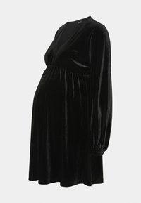 Robe de maternité en velours noir avec un décolleté en V, des manches longues bouffantes et une taille élastiquée, présentant une silhouette fluide.