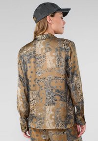 Lange mouw, gebloemd overhemd in goud en zwart, met paisley-ontwerpen. Glad materiaal met een kraag en knoopaccenten.