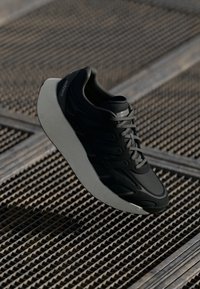 Juodos sportinės bateliai su lengvu dizainu, tinkliniais viršutiniais sluoksniais ir tekstūruotu padu. Išskirtiniai bruožai apima subtilią ženklinimą ir aerodinaminę formą.