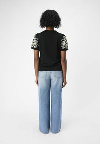 Svart kortärmad topp med dekorativa broderade blommönster på axlarna, i kombination med ljusblå vida jeans.