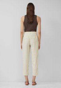 Lichtbeige cropped broek met een gladde textuur, voorzien van ri loops, twee achterzakken en een losse fit, in combinatie met bruine sandalen.