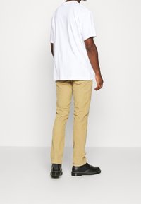 Camiseta de algodón blanca, de corte relajado, combinada con pantalones de pana beige. Unos zapatos de cuero negro con suela resistente completan el atuendo.