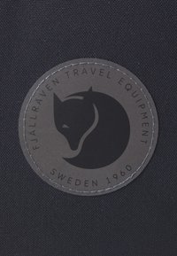 Black fabric background with a circular leather patch featuring a fox silhouette, "FJÄLLRÄVEN TRAVEL EQUIPMENT," and "SWEDEN 1960" text.