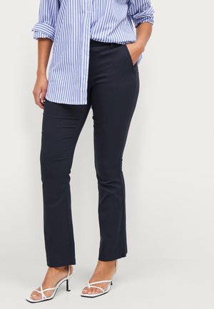 Navy broek met een slim fit en een lichte uitloop aan de zoom, gecombineerd met een gestreept blauw-wit overhemd met lange mouwen en witte hoge hakken.