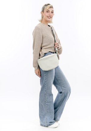 Borsa a tracolla grigia chiaro in pelle testurizzata con chiusura a zip. Indossata a tracolla, abbinata a un maglione beige e jeans a vita alta.