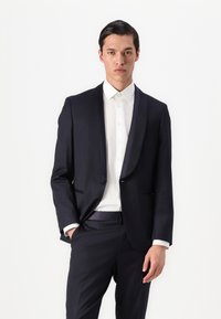 Námornícky tailored oblek so saténovými klopami, biela košeľa a nohavice rovného strihu. Hladká tkanina, navrhnutá na formálne príležitosti.