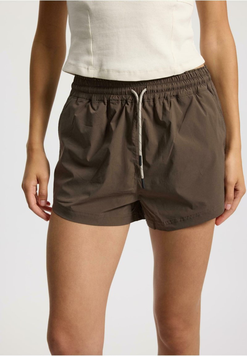 Pantalones cortos marrones, ligeros, con cintura elástica, cierre con cordón y bolsillos laterales. Textura suave, diseño casual.