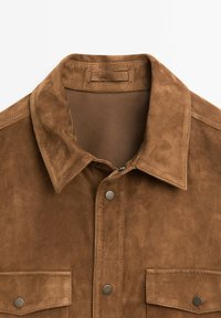 Braunes Wildlederhemd mit einem klassischen Kragen, zwei vorderen Taschen mit Druckknöpfen und einer glatten, strukturierten Oberfläche.