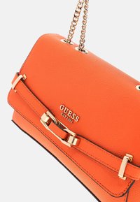 Borsa a mano in pelle arancione con superficie testurizzata, hardware dorato, tracolla a catena e fibbia decorativa. Logo del marchio ben visibile.