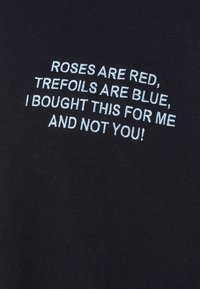 Zwarte t-shirt met witte geborduurde tekst: "ROZEN ZIJN ROOD, TREFOILS ZIJN BLAUW, IK HEB DIT VOOR MIJ GEKOCHT EN NIET VOOR JOU!" Glad stofoppervlak.