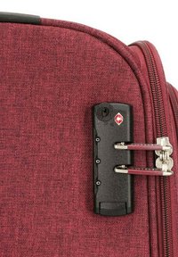 Valise en tissu texturé rouge avec un verrou TSA noir, une fermeture à glissière argentée et deux tirettes en métal. Dispose d'un design robuste pour garantir sa durabilité.