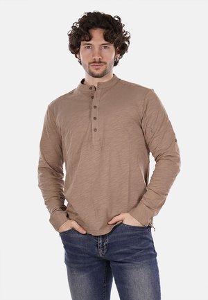 Maglietta henley marrone a maniche lunghe con tessuto strutturato, placket con tre bottoni e polsini a coste. Abbinata a jeans scuri.
