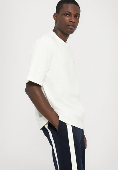 Camiseta de manga corta, de color blanco roto, hecha de tela suave, combinada con pantalones azul marino que tienen franjas laterales blancas y un corte relajado.