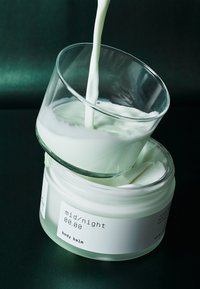 Hvit kroppsbalsam i en klar krukke, toppet med dryppende hvit krem. Moderne design med minimal tekstetikett i svart. Teksturert, glatt overflate.