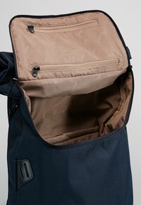 Námořnický batoh s hladkým povrchem. Otevřený interiér ukazuje béžovou podšívku se dvěma zipovými kapsami a několika přihrádkami pro organizaci.