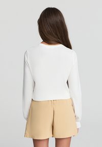Biała bluzka z długim rękawem i okrągłym dekoltem w połączeniu z beżowymi szortami. Tkanina wydaje się miękka i gładka, ma luźny krój i prosty design.