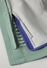 Kerrosmateriaali, jossa on vaaleanharmaa sileä kangas, mintunvihreä tehoste, violetti fleeceosuus ja kuvioitu verkkokangas alla.